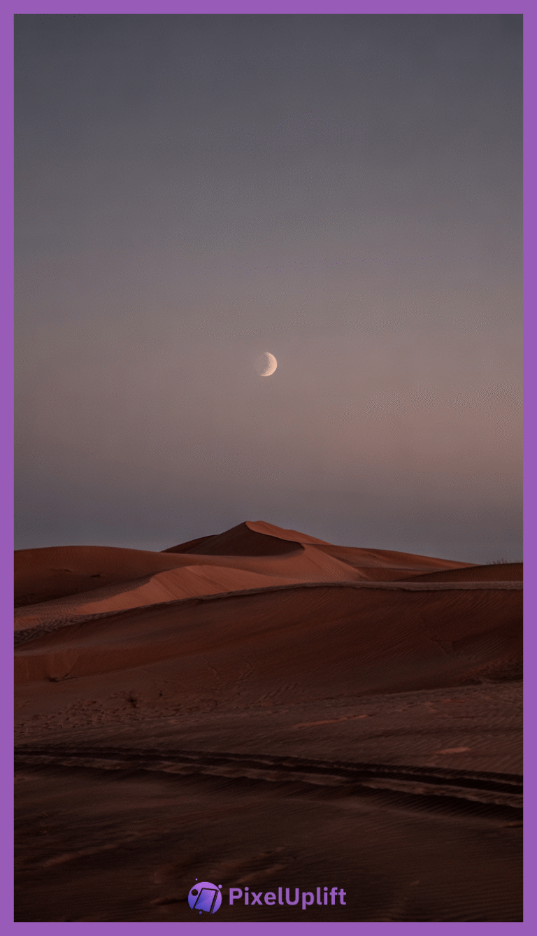 Serene desert landscape at twilight with reddish-brown sand dunes, tire tracks, footprints, and a half-moon in the clear sky